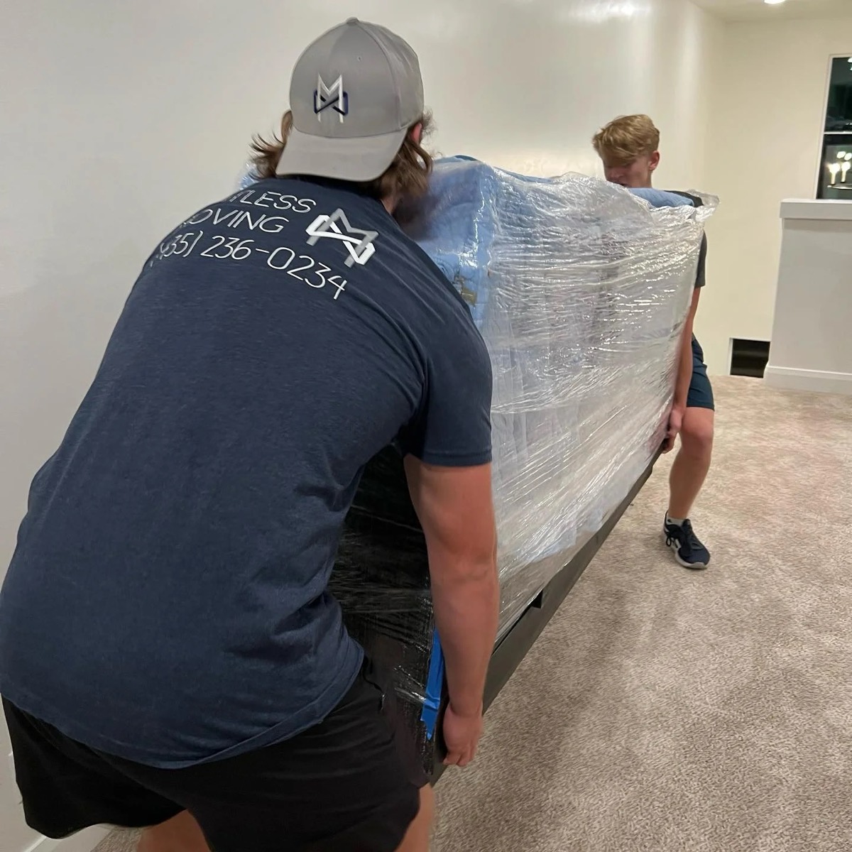 Two movers carrying a plastic-wrapped piece of furniture through a home