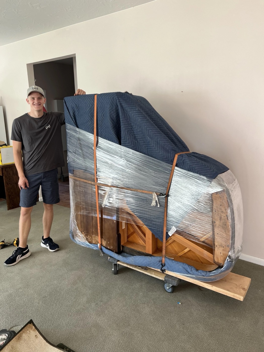 Grand piano wrapped in moving blankets and plastic on a piano board